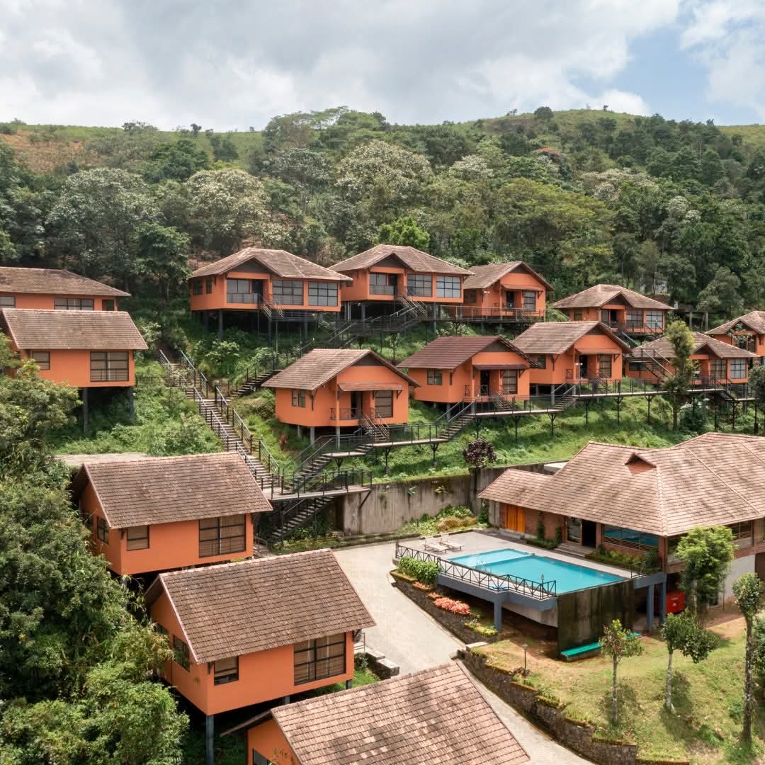 Aerial view of the hillside cottages stepping down to the infinity pool at Heyday Thazhvaram, Panchalimedu, Idukki, Kerala