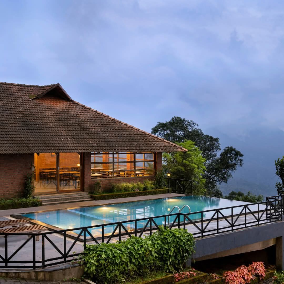 Infinity pool and brick cottage lit at blue hour above the cardamom valley at Heyday Thazhvaram, Panchalimedu, Idukki, Kerala